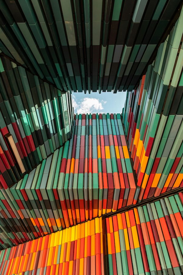 Colorful modern building facade with layered vertical panels in shades of green, orange, and red.