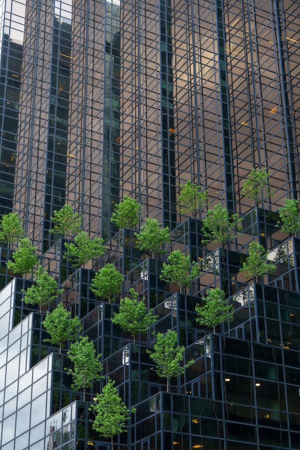 Modern high-rise building facade with balconies filled with trees and greenery, blending architecture and nature.